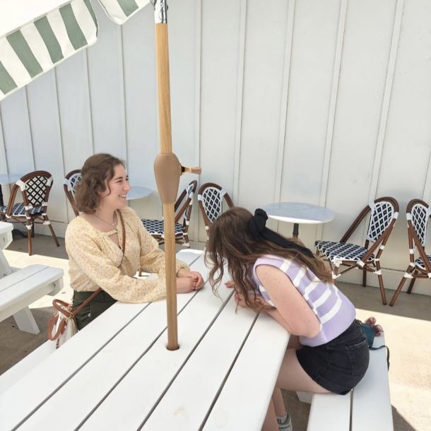 two girls sitting at a white picnic table at a cafe laughing under an umbrella
