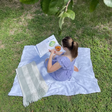 Young woman having a picnic drinking tead while reading The Little Teacup Children's book