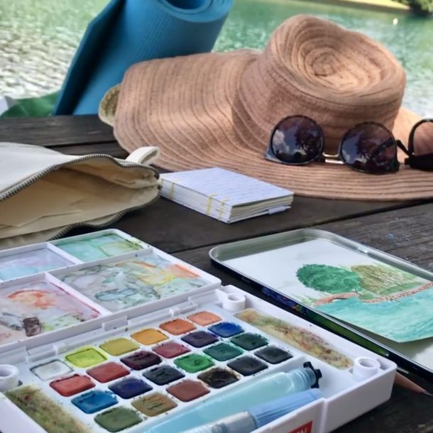 Travel watercolor kit and sunhat sitting on a picnic table