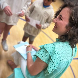 Smiling author in aqua shirt signing autographs for students in school gym