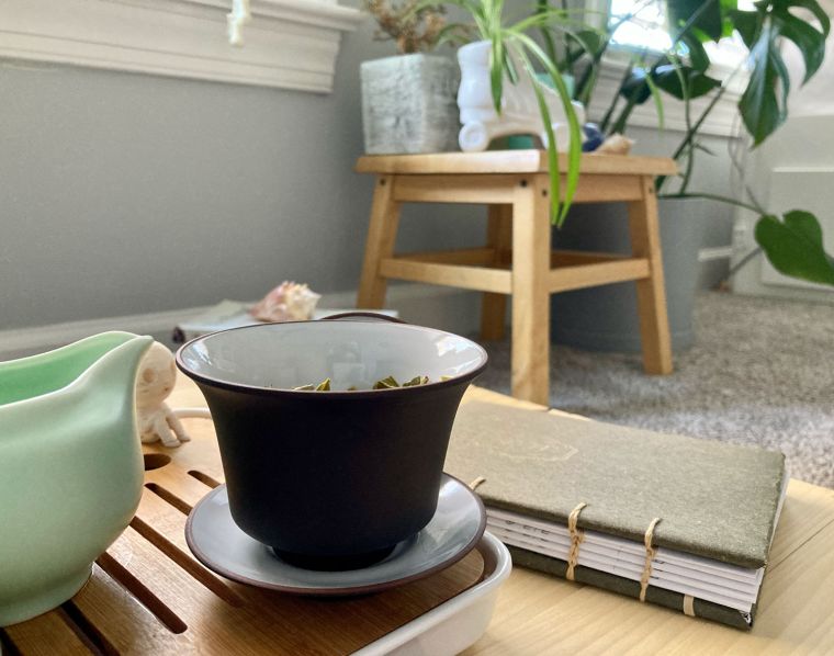 Tea in a personal gaiwan with tea tasting journal in a sunroom